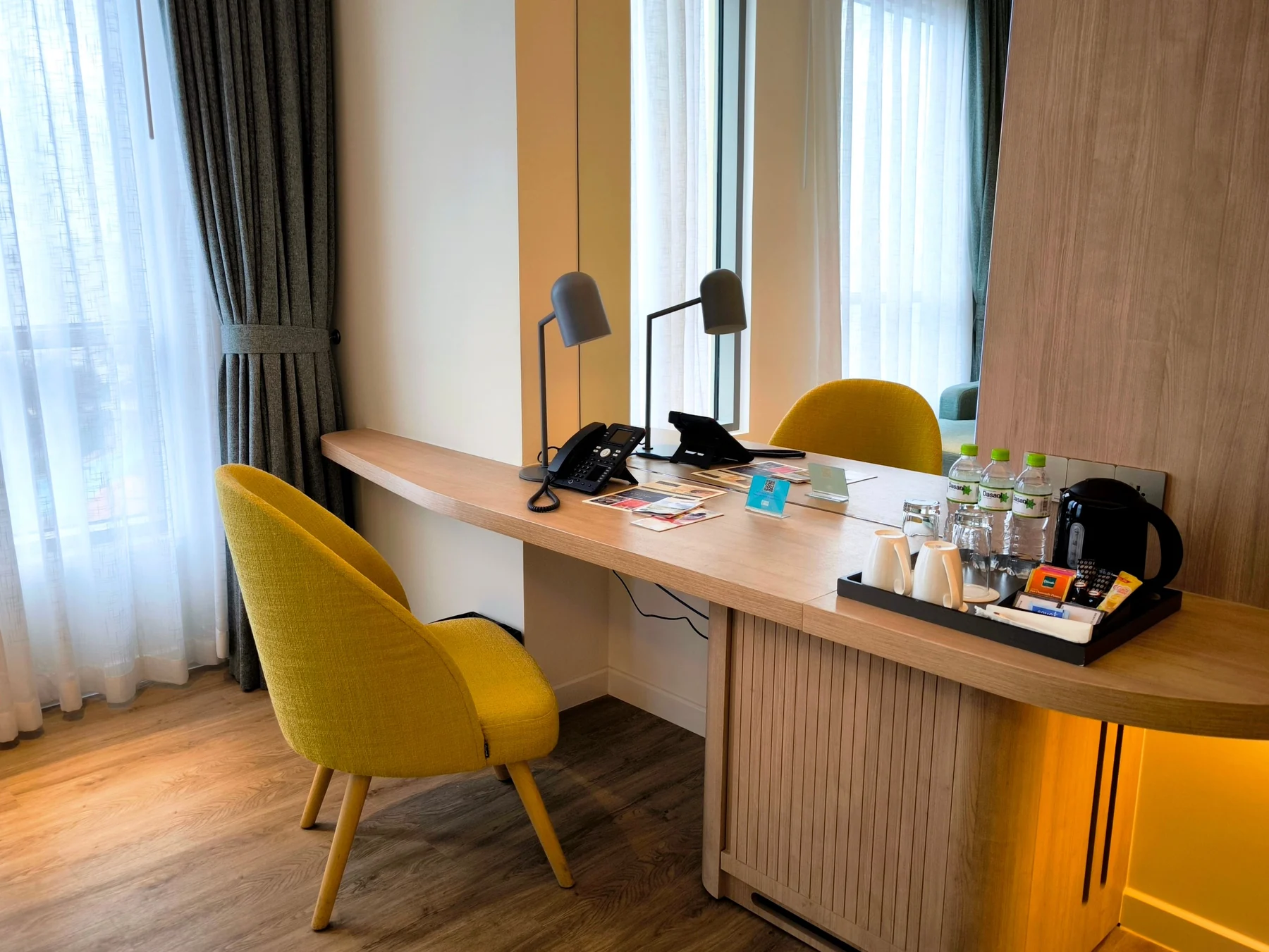 A wooden desk, chair and mirror beside a hotel-room window